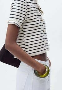 Top a maniche corte a righe in crema e navy, con bottoni dorati. Abbinato a jeans bianchi a vita alta e un accessorio circolare verde.