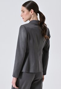 Blazer grigio su misura con una texture del tessuto liscia, vestibilità slim e dettagli delle cuciture discreti sulla schiena. Presenta un colletto classico e maniche lunghe.
