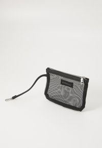 Černý síťovaný pytlík se zipem, vybavený smyčkou na držení a značkovým štítkem. Hladký povrch, obdélníkový tvar a lehká konstrukce.