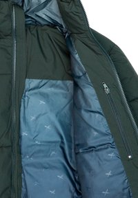 Interno di una giacca a vento verde scuro, con una fodera blu liscia e un motivo sottile. Visibile tasca laterale con zip e chiusura frontale con zipper.