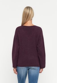 Pull en maille violet foncé avec un large décolleté et des épaules tombantes. Présente des poignets et un ourlet côtelés, associé à un jean bleu.