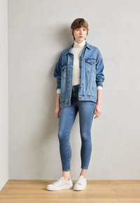 Jeansjakke med løs passform, lyseblå nyanse, to brystlommer, kombinert med tettsittende lyseblå jeans og hvite joggesko.