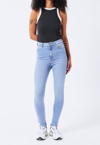 Czarny top na ramiączkach z białym obszyciem, zestawiony z jasnoniebieskimi, obcisłymi jeansami z wysokim stanem. Modelka ma na sobie białe sportowe trampki.