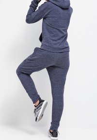Sweat à capuche bleu marine et joggings assortis fabriqués en tissu texturé, avec une poche kangourou et des poignets élastiques. Des chaussures de sport noires complètent la tenue.