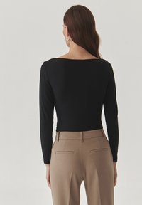 Zwart langemouwen top met een ronde hals, gecombineerd met beige op maat gemaakte broek met achterzakken en een gladde stofstructuur.