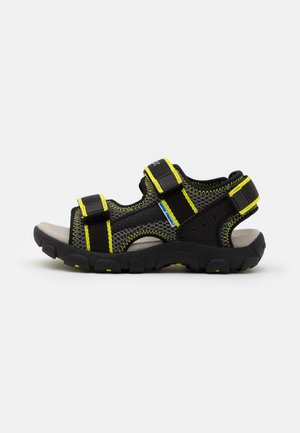 Sandalias al aire libre en negro y gris con acentos amarillos, que cuentan con una parte superior de malla transpirable, correas ajustables y una suela de goma texturizada.