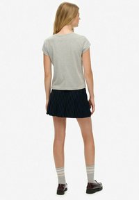 T-shirt grigio a maniche corte, gonna nera a pieghe con righe verticali, calze grigio e bianche a righe, scarpe nere, viste da dietro.