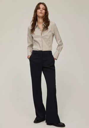 Donna che indossa una camicia button-up a righe bianche e beige infilata in pantaloni culotte neri a vita alta, con mocassini neri.