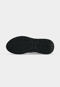 Semelle de chaussure en caoutchouc noire avec des motifs de rainures profondes et le nom de la marque "BOSS" embossé au centre.