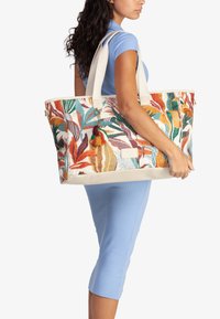 Grande borsa a tracolla con un vivace motivo a foglie in arancione, verde e blu. Realizzata in tessuto resistente con manici color crema e una frangia decorativa.