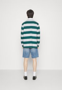 Gestreepte lange mouwen shirt in teal en grijs, gecombineerd met lichtblauwe denim shorts. Het model draagt zwarte schoenen en witte sokken.