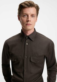 Mørkebrun skjorte med knapper i et struktureret stof, med krave, to brystlommer og matchende knapper. Skræddersyet pasform.