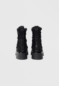 Botas de tobillo negras con un upper de tela texturizada, un cuello acolchado y una suela de plataforma gruesa. Los detalles incluyen la marca DKNY en el talón.