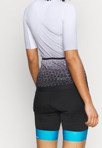 Czarne spodenki rowerowe z niebieskim akcentem przy krawędzi, w połączeniu z szarą bluzką z krótkim rękawem z geometrycznym wzorem i kieszenią na zamek.