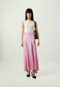 Hvit strikket topp uten ermer kombinert med et flytende rosa sateng maxiskjørt med høy-lav søm, svarte hæler, og en svart håndveske.