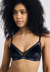 Black bra with a velvet texture, sheer accents, and a v-shaped design. Features adjustable straps and a branded underband.