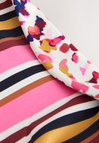 Multifarvet stof med markante striber i pink, brun, marineblå og guld med et blomsteraccent i hvide, pink og gule teksturer.