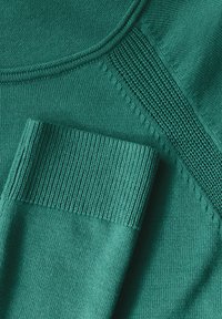 Maglione lavorato a maglia color teal con scollo rotondo, caratterizzato da polsini a coste e una transizione testurizzata tra diversi modelli di punto.