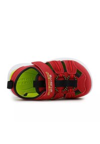 Zapatilla deportiva roja con acentos en negro y verde. Cuenta con una parte superior sintética, una correa ajustable de Velcro y una plantilla acolchada con un patrón texturizado.