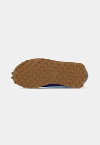 Sola de sapato com um padrão de aderência de borracha castanha, composto por pequenos pinos quadrados, apresentando o logotipo da Nike no centro.