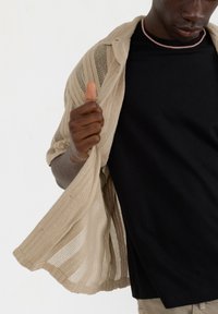 Beige åbenstrikket cardigan båret over en sort t-shirt. Cardiganen har et tekstureret mønster og flydende ærmer med en løs pasform.