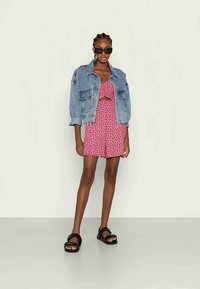 Jaqueta de ganga sobre um top curto floral rosa e calções combinando, acompanhada de sandálias pretas. O conjunto apresenta um design casual e um corte descontraído.