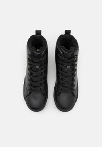 Zapatillas negras de caña alta con exterior de cuero liso, forro de felpa texturizada y cordones negros. Incluyen una lengüeta para facilitar su uso.