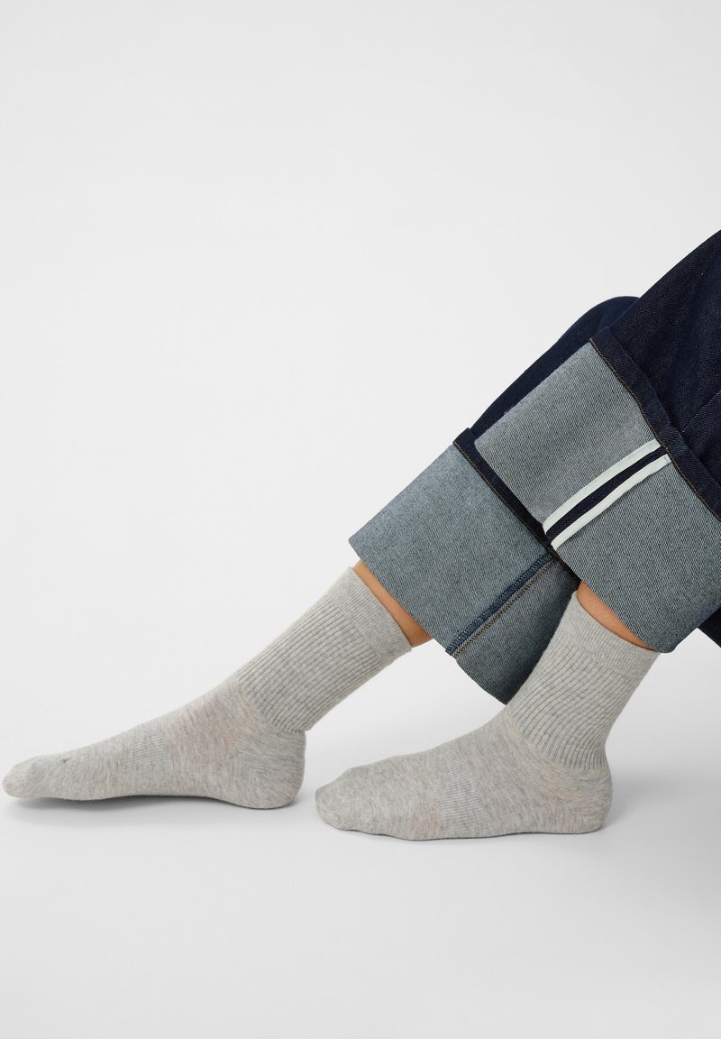 Personne portant des chaussettes côtelées gris clair et un jean bleu foncé retroussé sur un fond clair uni.