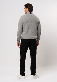 Pilkas megztinis su aukštu apykakle, turintis raudoną, baltą ir mėlyną juostą gale. Suderintas su juodomis kelnėmis ir baltais batais.