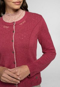 Rosa gestrickte Jacke mit einem Kragen aus Spitze, Knöpfen auf der Vorderseite und kunstvollen gewebten Mustern an den Ärmeln und am Saum.