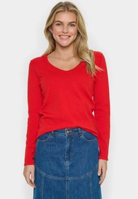 Pull rouge à manches longues en V, en tricot doux, associé à une jupe en denim avec un design en patchwork et une fermeture à boutons à l'avant.