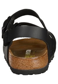 Musta sandaali säädettävällä hihnalla, korkkipohjalla ja teksturoidulla kumipohjalla. Sisältää leikkauksen takana ja minimalistista metalliosaa.