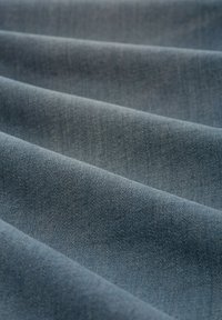 Denim audums mīkstā zila tonī, ar nedaudz strukturētu virsmu, kurā redzami izpītās šķiedras un smalkas krāsu variācijas.