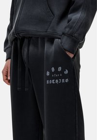 Zwarte hoodie met een voorzak en trekkoord, gecombineerd met donkere trainingsbroek met een geprinte grafiek "GOD for NOTHING" in contrasterend grijs.