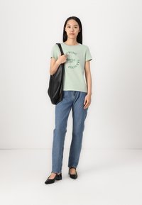 Grønn bomulls T-skjorte med trykket tekst, blå rette jeans, og svart skinn tote bag. Svart spiss tå hæler. Enkelt design og passform.