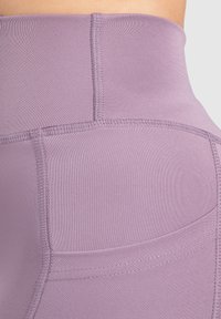 Hoge taille, slimfit legging gemaakt van gladde, rekbare stof in een zachte lavendelkleur. Bevat versterkte stiksels en een zijzak.