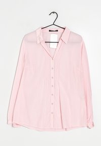 Blusa de manga larga color rosa claro con cuello, tapeta frontal, pequeños botones y detalles plisados. Tela ligera y transparente con un ajuste relajado.