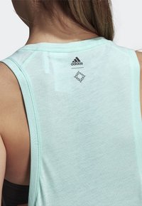 Top sin mangas verde menta claro con un escote redondo, hecho de una tela texturizada. Presenta un logo de Adidas y un diseño geométrico en la parte posterior.