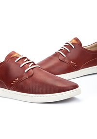 Zapatos de cuero en rojo oscuro con un diseño perforado. Presentan cordones blancos y una suela blanca en contraste. Detalles en color marrón claro.