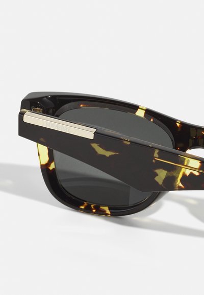 Ochelari de soare din tortoise cu un model negru și ambră, lentile dreptunghiulare și un braț din metal cu accente aurii, inscripționat cu "Burberry".