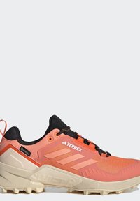 Buty trailowe Terrex w kolorze pomarańczowym i czarnym, z teksturowaną cholewką, sznurowadłami, wzmocnionym heel i solidną podeszwą zapewniającą przyczepność.