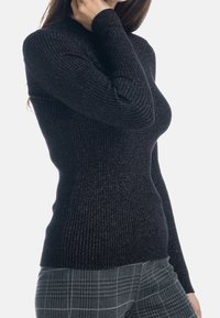 Un pull turtleneck noir côtelé avec un subtil éclat métallique, doté de manches longues et d'une coupe ajustée, associé à un pantalon à carreaux.