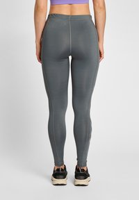 Höga, åtsittande leggings i dämpad grå färg, tillverkade av ett mjukt, elastiskt tyg med kontrasterande sömmar och sidofickor.