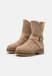 Vihreät mokkanahkaiset nilkkurit, joissa on teksturoitu pinta, tekoturkista vuori ja koristeellinen remmi, jossa on hopeinen solki. Kumi-ulkopohja.