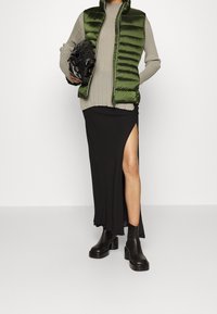 Grøn polstret vest, grå ribbet sweater, sort maxiskørt med sideslids, sorte ankelstøvler og en sort taske med tekstureret design.