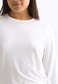 Weißes Langarmshirt aus weicher Stoffqualität, mit rundem Ausschnitt und einer glatten, taillierten Silhouette.