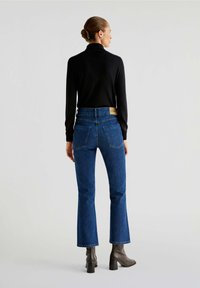 Dark blue flared jeans with a high waist, featuring two back pockets and a tan leather label at the waistband, paired with a black fitted sweater.