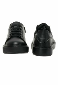 Zapatillas de cuero negro con punta redonda, suela de goma texturizada, cierre con cordones en la parte delantera y costuras blancas en contraste a lo largo de la parte superior.