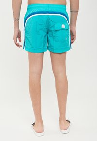 Pantaloni da bagno turchesi con vita elasticizzata, strisce laterali bianche e una tasca posteriore con patch del logo. Tessuto leggero e liscio.