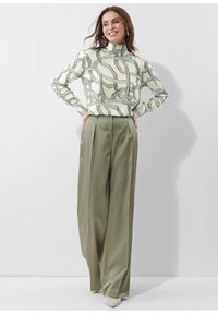 Langarmrollkragenpullover in Creme mit grünen abstrakten Linien, kombiniert mit hochtaillierten, weit geschnittenen olivgrünen Hosen und nudefarbenen hohen Schuhen.